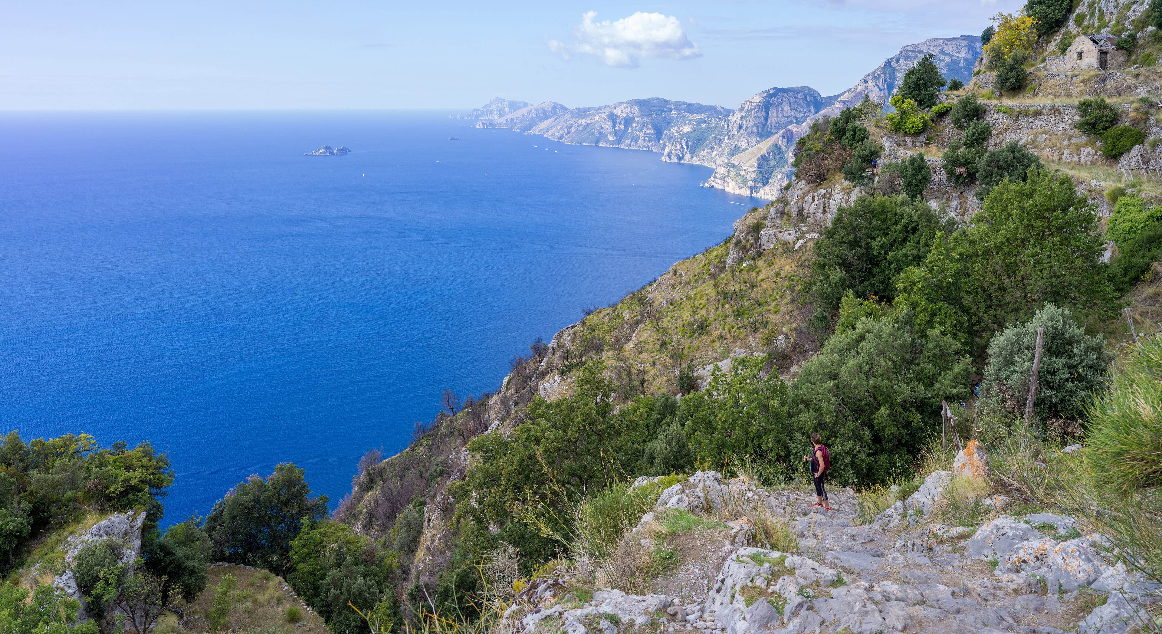 A hiker on the rocky Path of the Gods high above the sea, with the coastline running out towards Capri